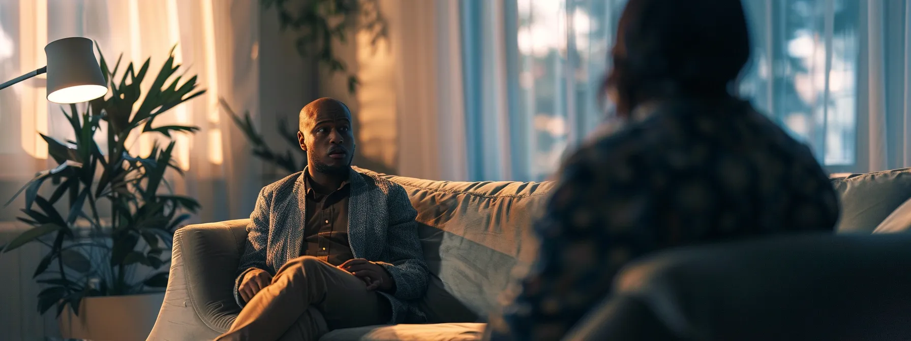 a person seated on a couch listening intently to a therapist during a counseling session.